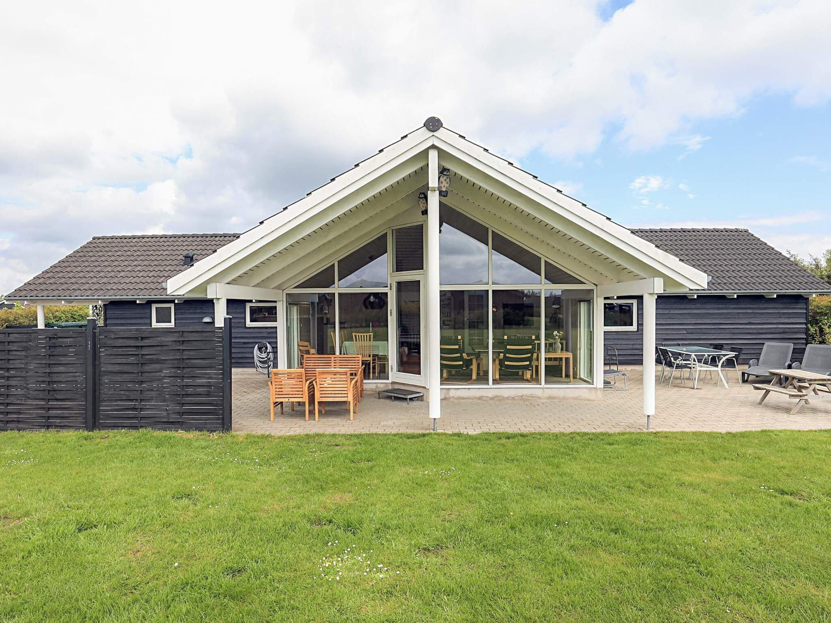 A modern house with a covered patio, a fenced yard, and a grassy lawn.