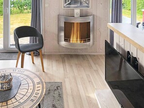 A modern living room with a fireplace, a dining area with a round table, and a large window offering a view of the outdoors.
