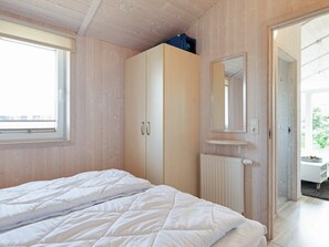 A bedroom with a bed, wooden wardrobe, a mirror, and a window.