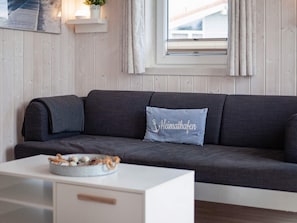 Una sala de estar moderna con un sofá gris, un cojín decorativo, una mesita con un cuenco y una ventana con cortinas.