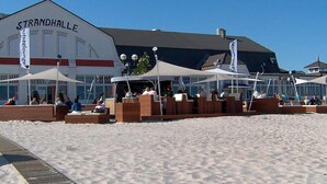 Ein Restaurant direkt am Strand mit Außenbereich und einem Gebäude mit der Aufschrift 'STRANDHALLE'.