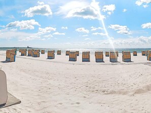A beach with rows of beach chairs and umbrellas, a pier in the background, and a clear sky.