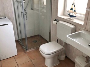A bathroom with a toilet, a shower enclosure, a sink, and a small window with a sailboat decoration.