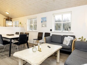 A modern living room with a dining area, large windows, and a kitchen in the background. - Stunning Holiday Home in Hirtshals with Hot Tub (Hirtshals)