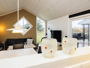 A modern interior with a white table, two decorative glasses, a hanging light fixture, and a view of the outdoors. - Stunning Holiday Home in Hirtshals with Hot Tub (Hirtshals)