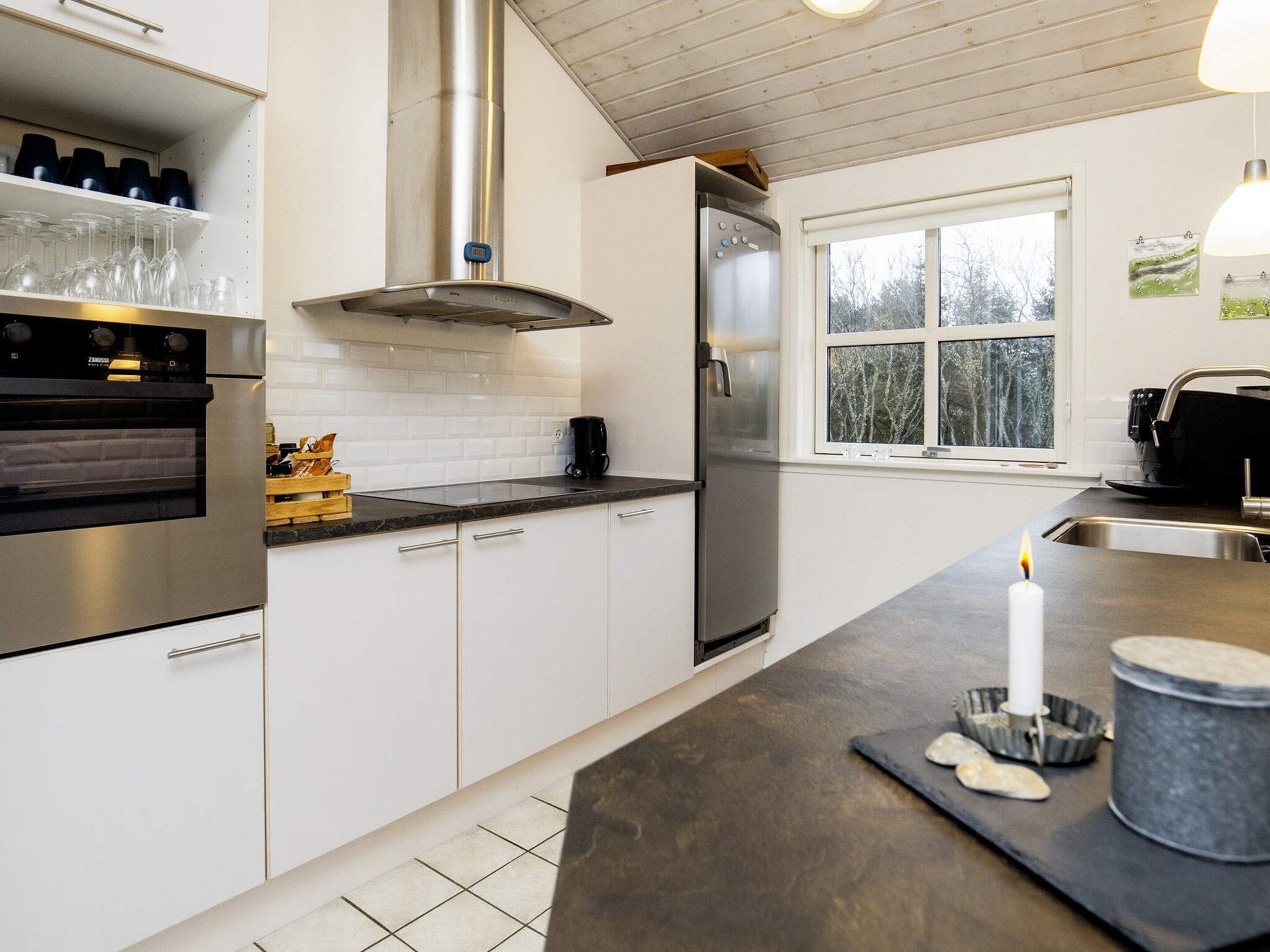 A modern kitchen with white cabinets, stainless steel appliances, a large window, and a candle on the counter.
