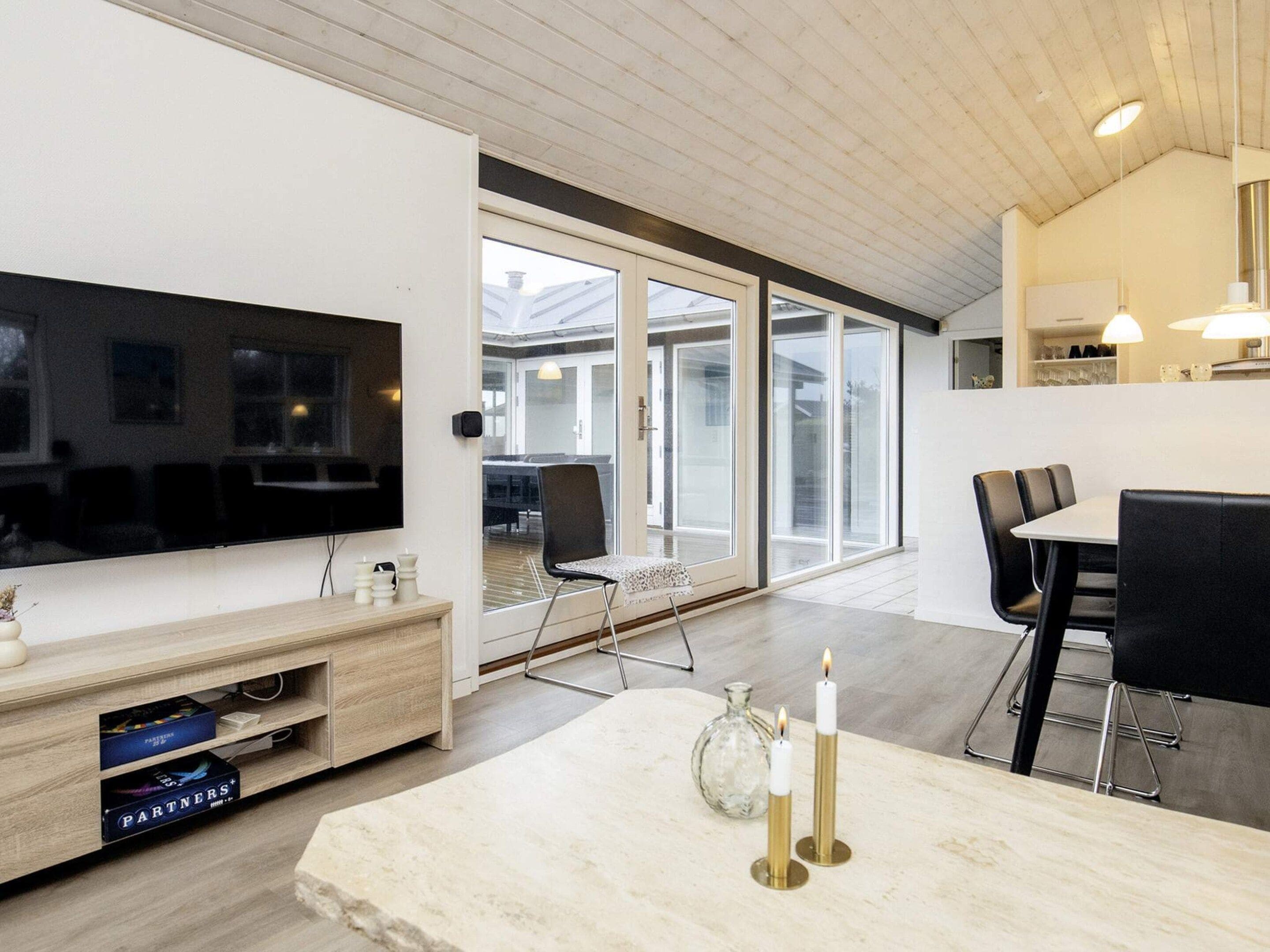 A modern living room with a flat-screen TV, a dining area with a table and chairs, and a large sliding glass door leading to an outdoor patio.