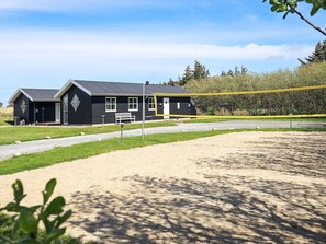 A black building with a gravel driveway and a bench in front.