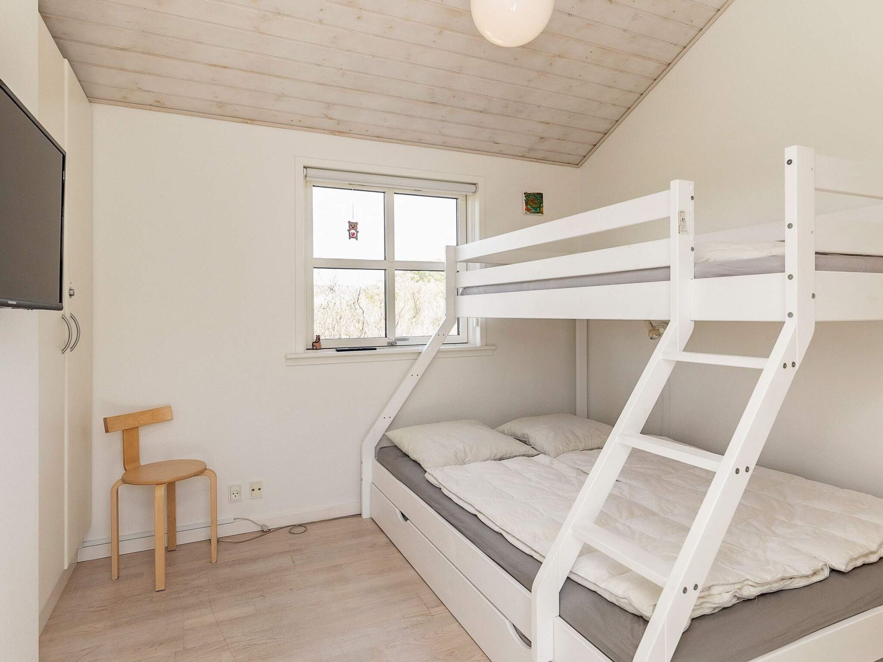 Un letto a castello con finestra, una sedia e un tavolino in una stanza con pavimento in legno e pareti bianche.