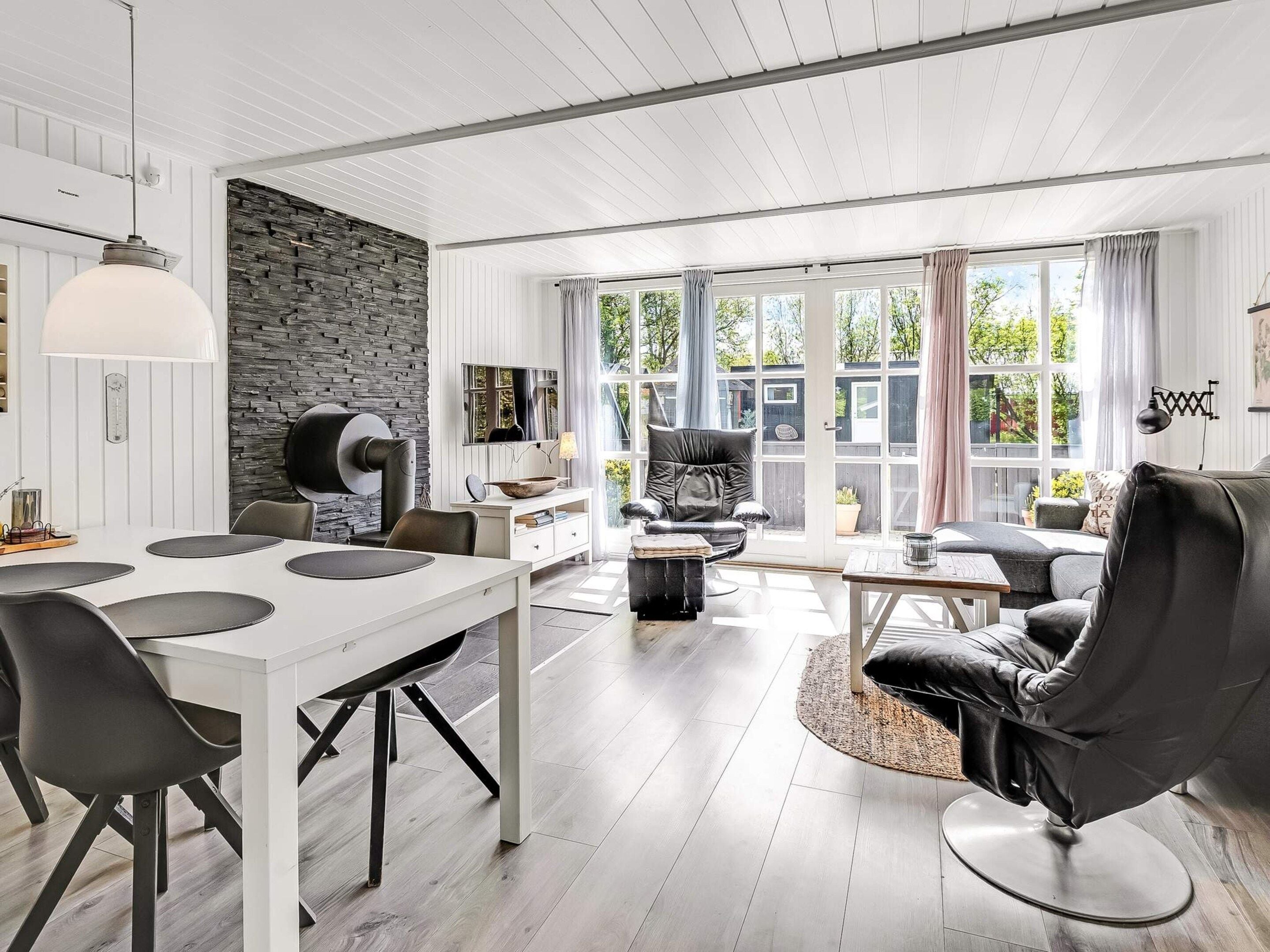 A modern living room with a dining area, stone wall, and large windows.