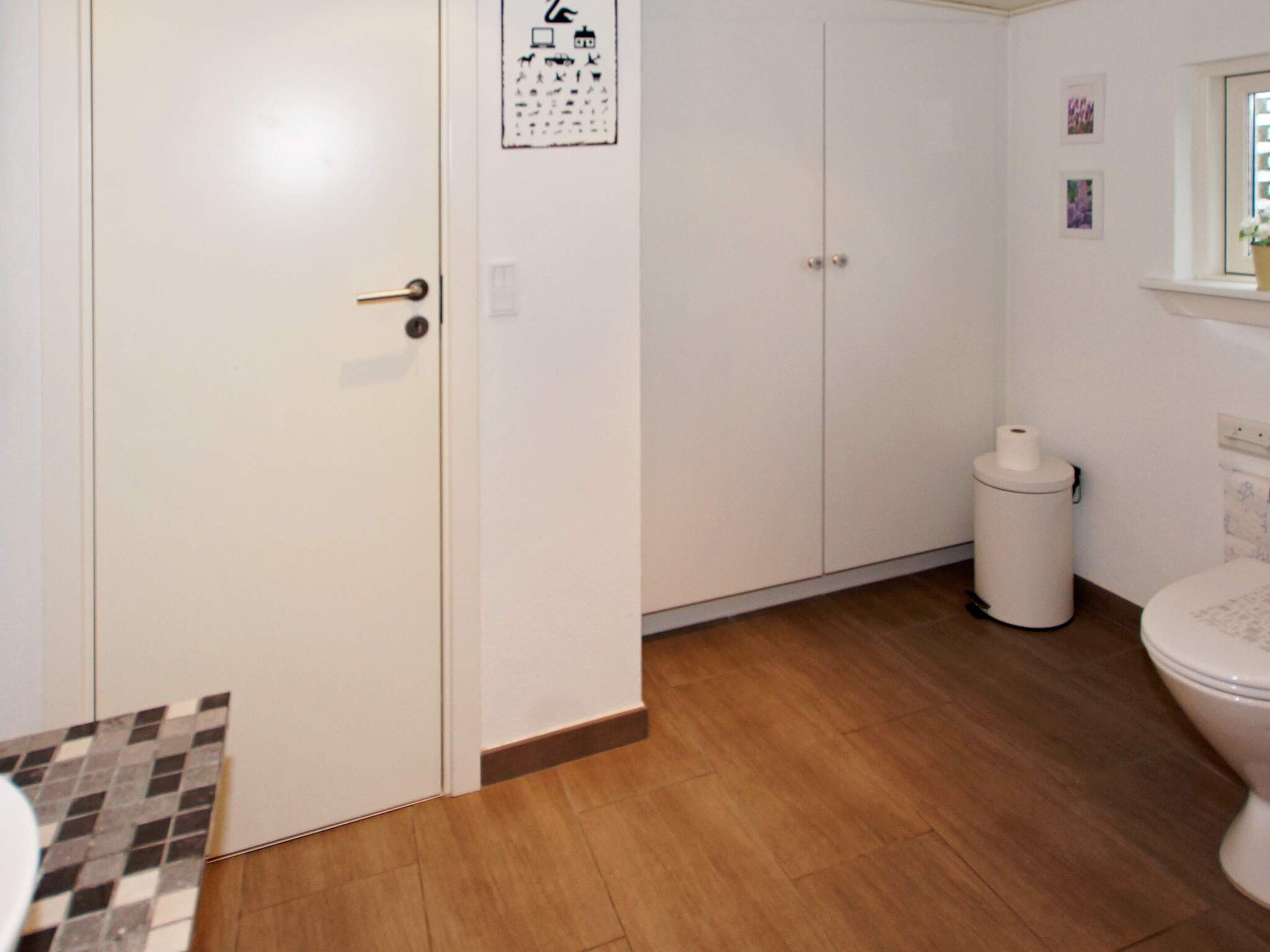Une salle de bain équipée de toilettes, d’une poubelle et d’un meuble avec une porte.