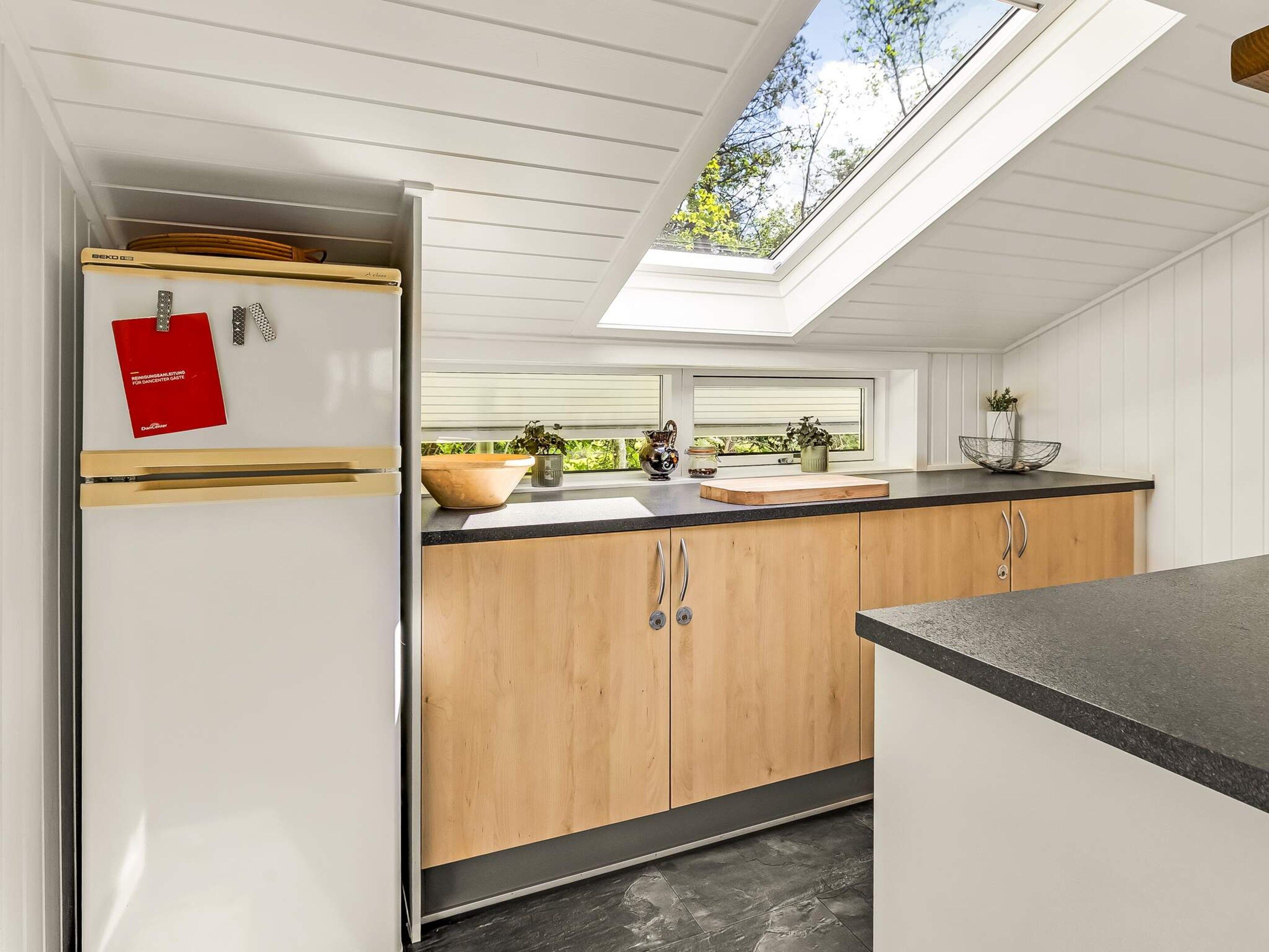 A modern kitchen with wooden cabinets, a black countertop, and a skylight above the sink.