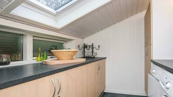 A modern kitchen with a skylight, wooden cabinets, a large bowl on the counter, and a washing machine.