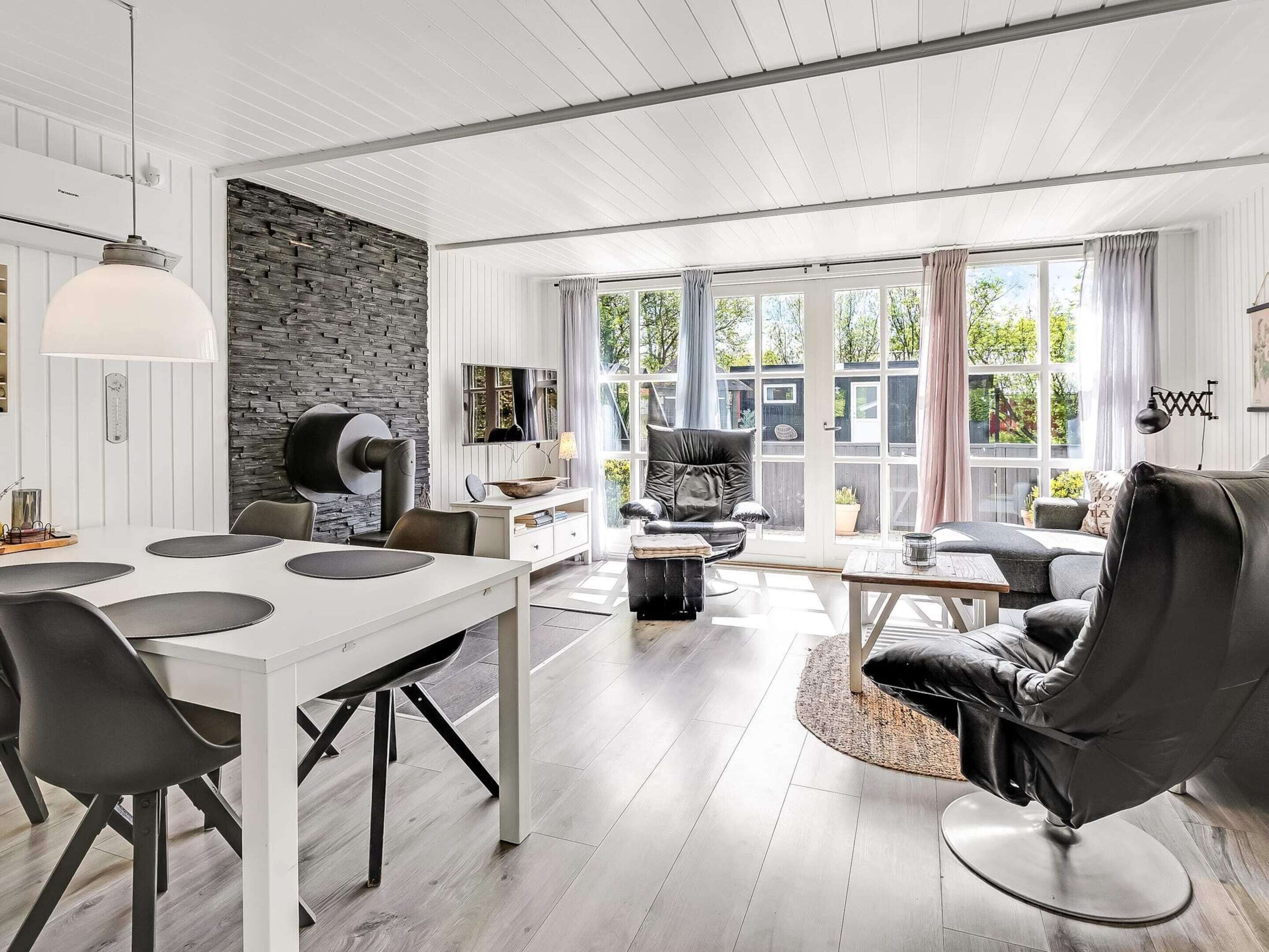A modern living room with a dining area, stone wall, and large windows.