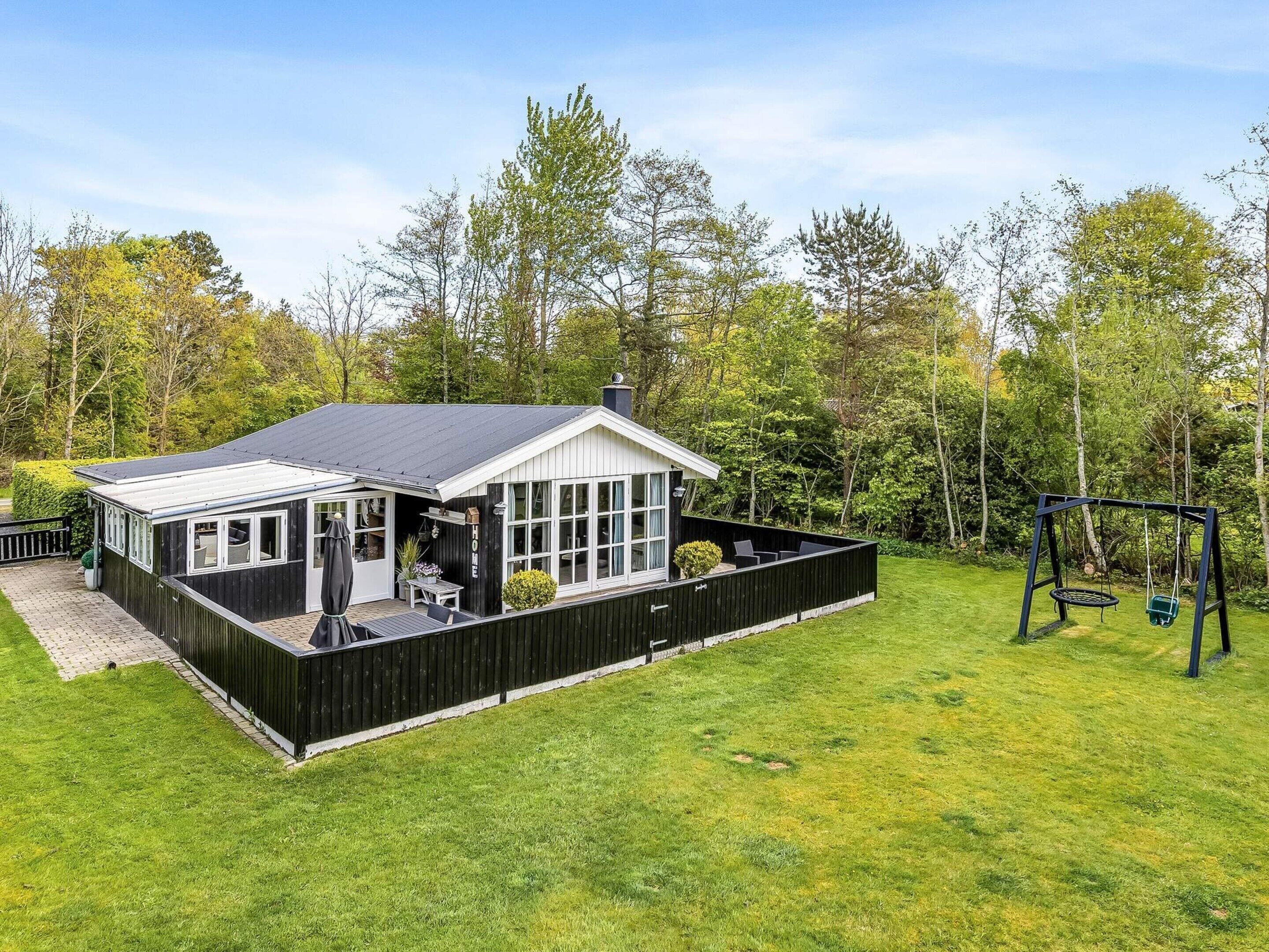 A house with a covered patio, a swing set, and a well-maintained lawn.
