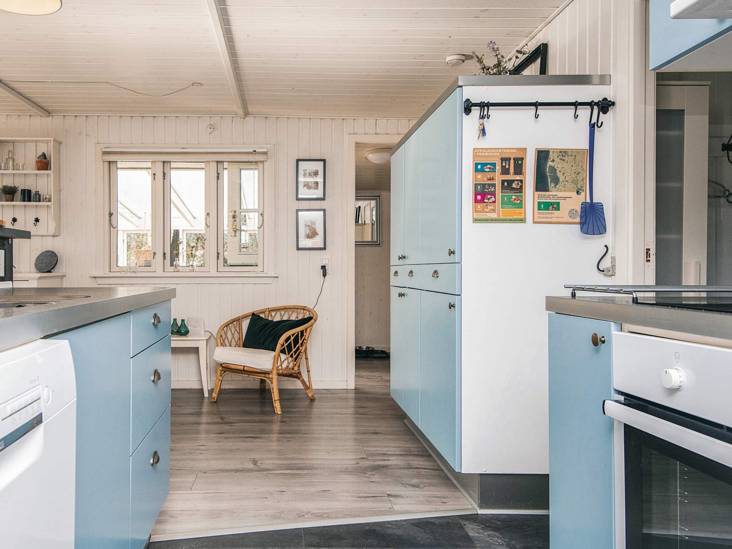 A kitchen with light blue cabinets, a wicker chair, and a window with a view.