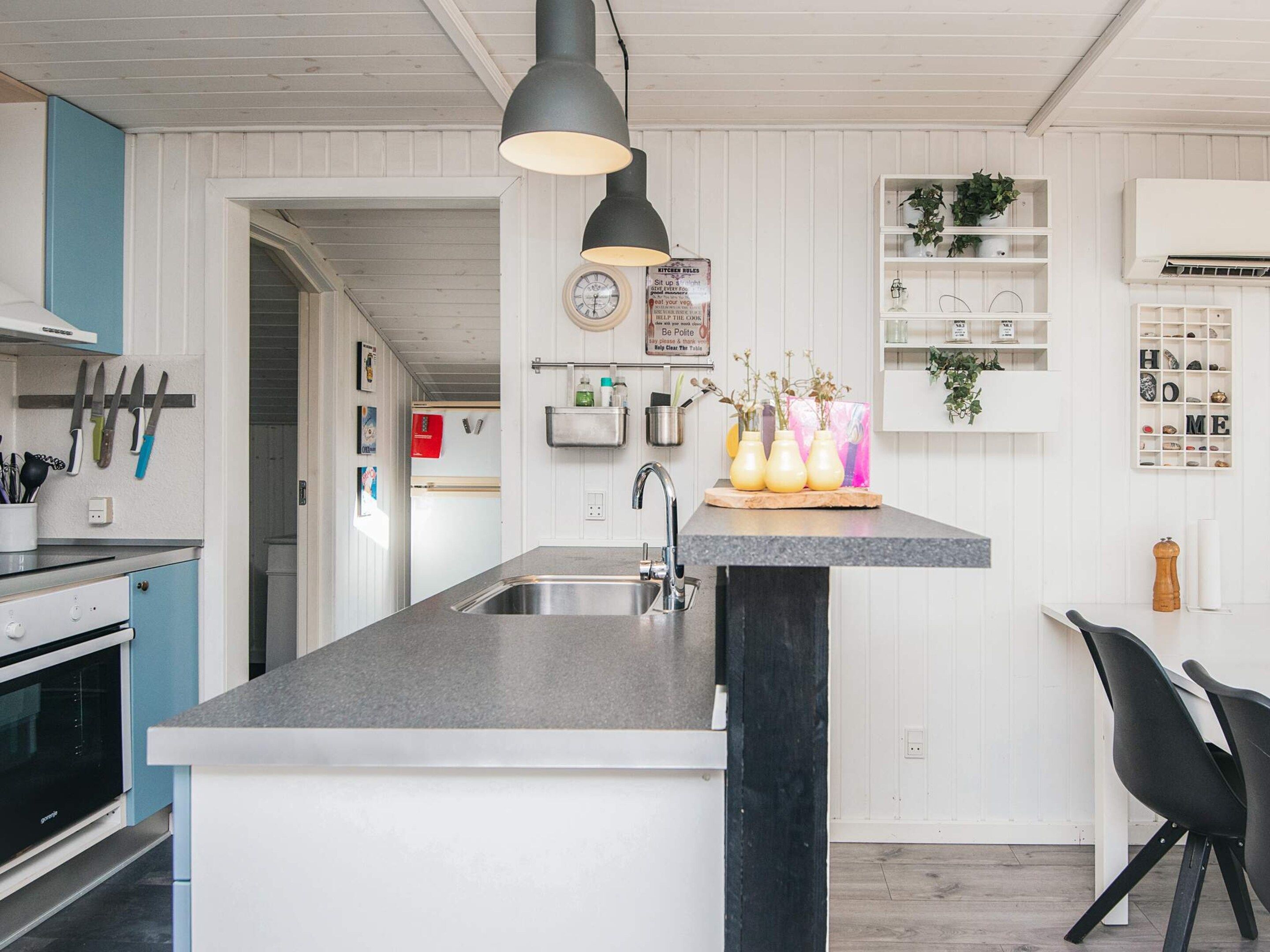 A modern kitchen with a central island, a built-in oven, and a hanging light fixture.