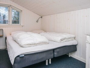 A single bed with a grey frame and white bedding in a room with white paneled walls and a window.