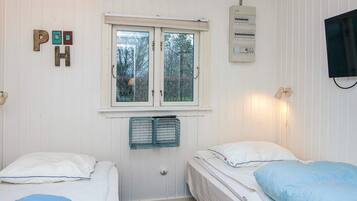 A room with two beds, a window, a wall-mounted heater, and a television.