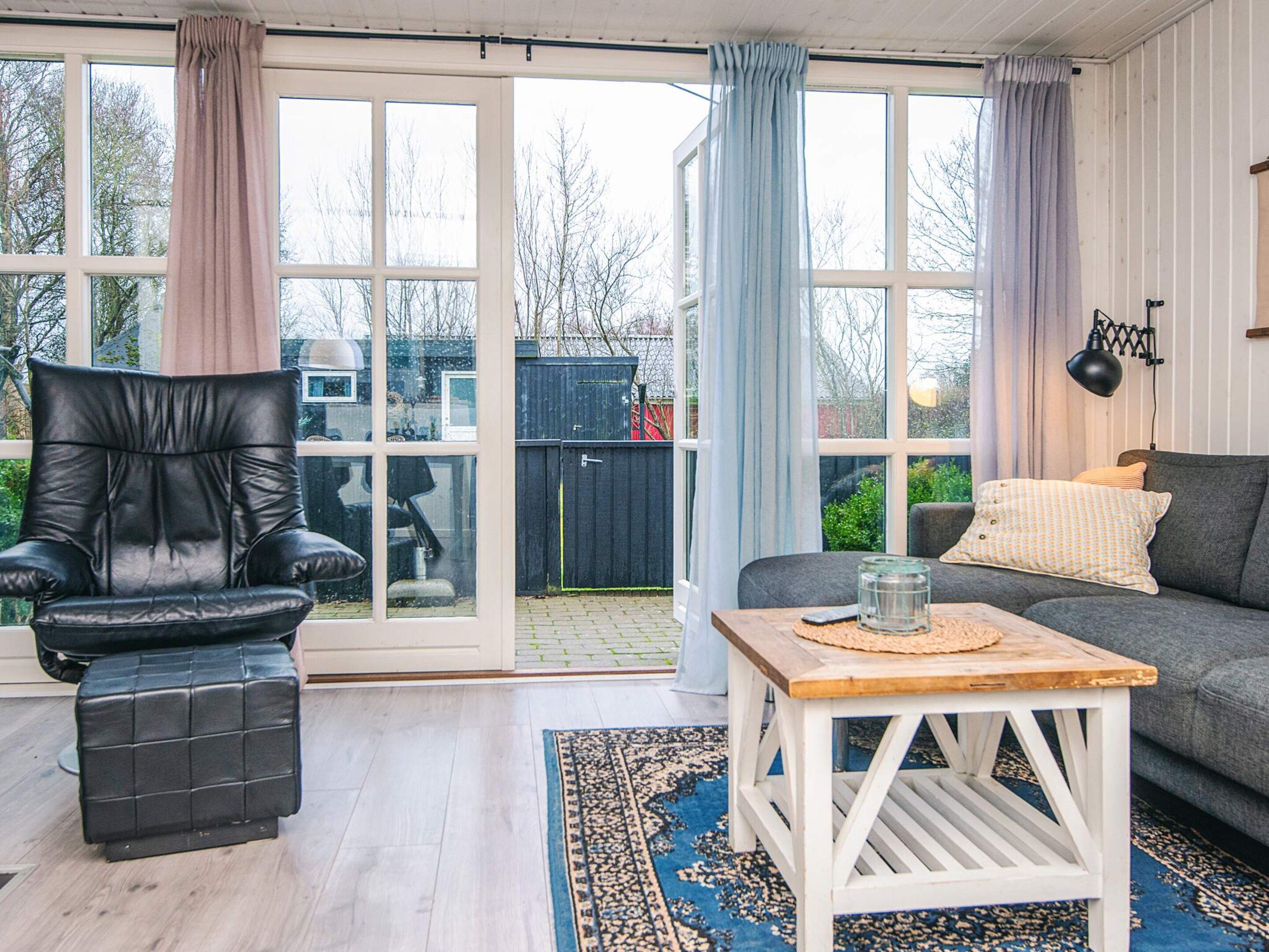 Un salon avec un fauteuil en cuir, un canapé gris, une table basse en bois et un tapis à motifs.
