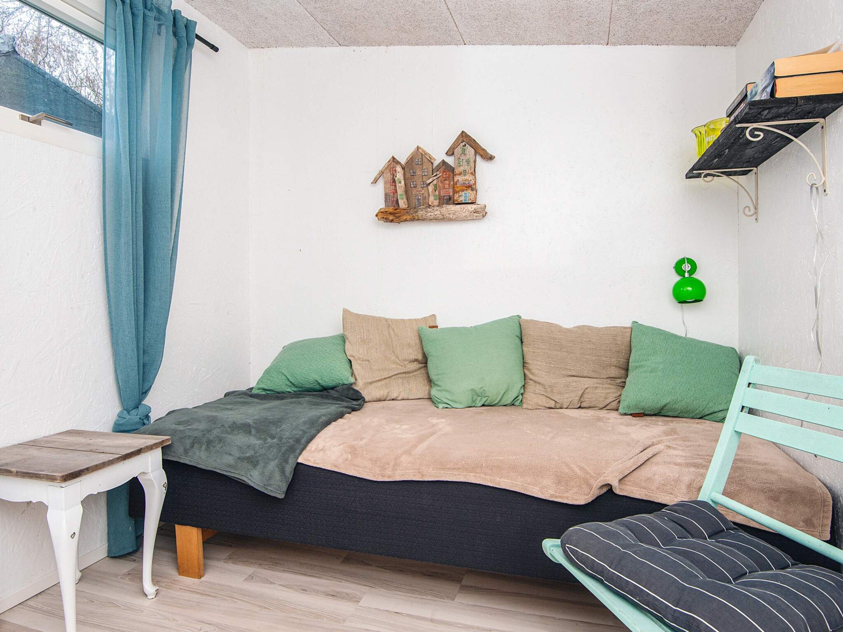 A cozy bedroom with a bed, a small table, a green lamp, and a shelf with books.