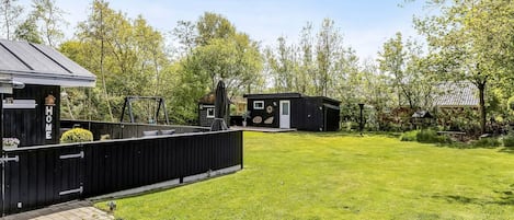 A residential property with a fenced backyard, a small house, and a wooden deck.