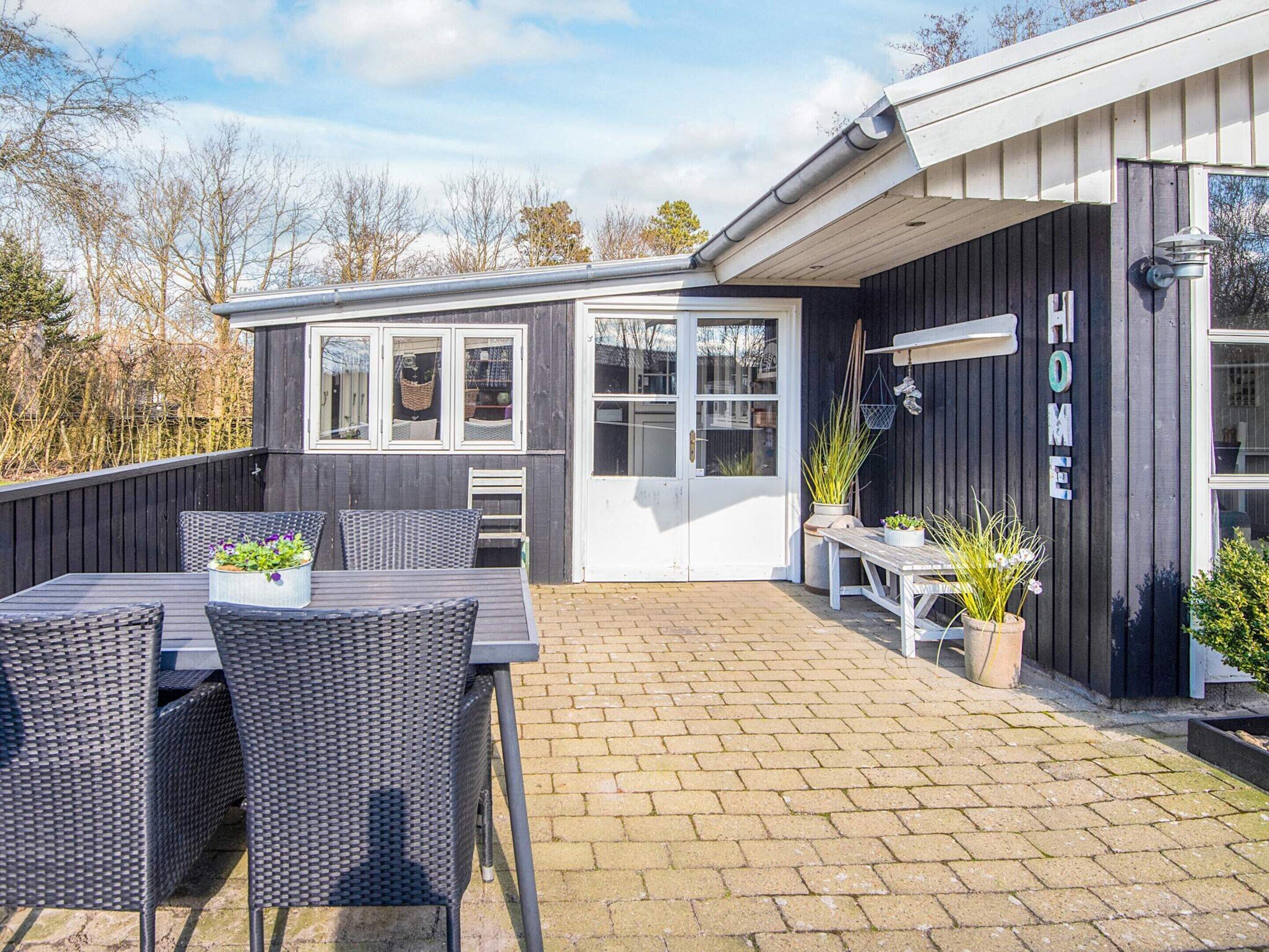 Un patio exterior moderno con una mesa y sillas de comedor, una zona de estar pequeña y una construcción de madera con un letrero que dice 'HOME'.