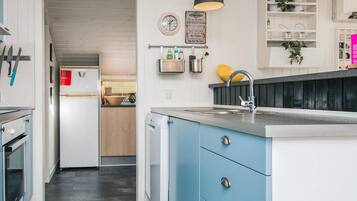 A kitchen with a blue cabinet, a sink, a clock, and a sign with kitchen rules.