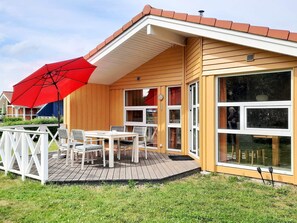 A wooden house with a covered patio, white-framed windows, and a red umbrella. - Holiday Home in GrÃ¶mmitz (Groemitz)