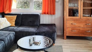 A modern living room with a sectional sofa, a round coffee table, and a wooden cabinet with glassware. - Holiday Home in GrÃ¶mmitz (Groemitz)