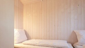 A room with two beds against a wooden wall, one with a mattress and pillows, and the other partially visible. - Holiday Home in GrÃ¶mmitz (Groemitz)