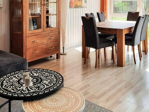 A dining area with a wooden table and chairs, a cabinet with glass doors, and a patterned rug. - Holiday Home in GrÃ¶mmitz (Groemitz)
