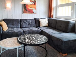 A modern living room with a sectional sofa, a round coffee table, and a painting on the wall. - Holiday Home in GrÃ¶mmitz (Groemitz)