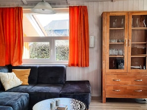 Ein Wohnzimmer mit einer dunklen Couch, einem runden Couchtisch und einer Holzkommode mit Glastüren.
