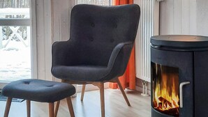 A room with a modern chair and ottoman, a wood-burning stove, and a view of a snowy landscape through the windows. - Holiday Home in GrÃ¶mmitz (Groemitz)