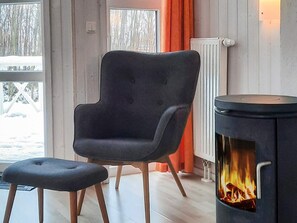 Ett rum med en modern fåtölj och ett tillhörande fotstöd, en vedkamin och utsikt över ett snötäckt landskap genom fönstren.