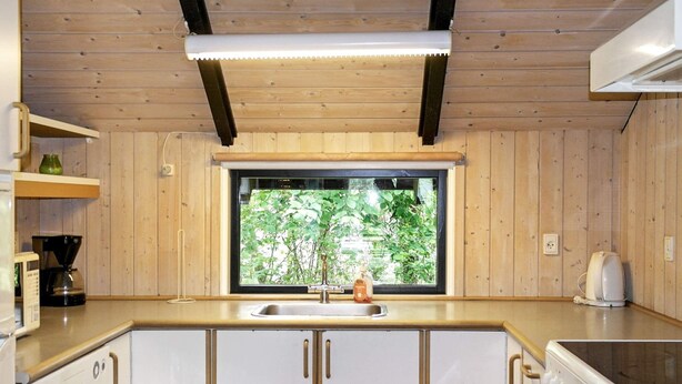 A kitchen with wooden cabinets, a sink, a window with a view of greenery, and a coffee maker. - 8 Person Holiday Home in Vaeggerlose-by Traum (Vaeggerlose)