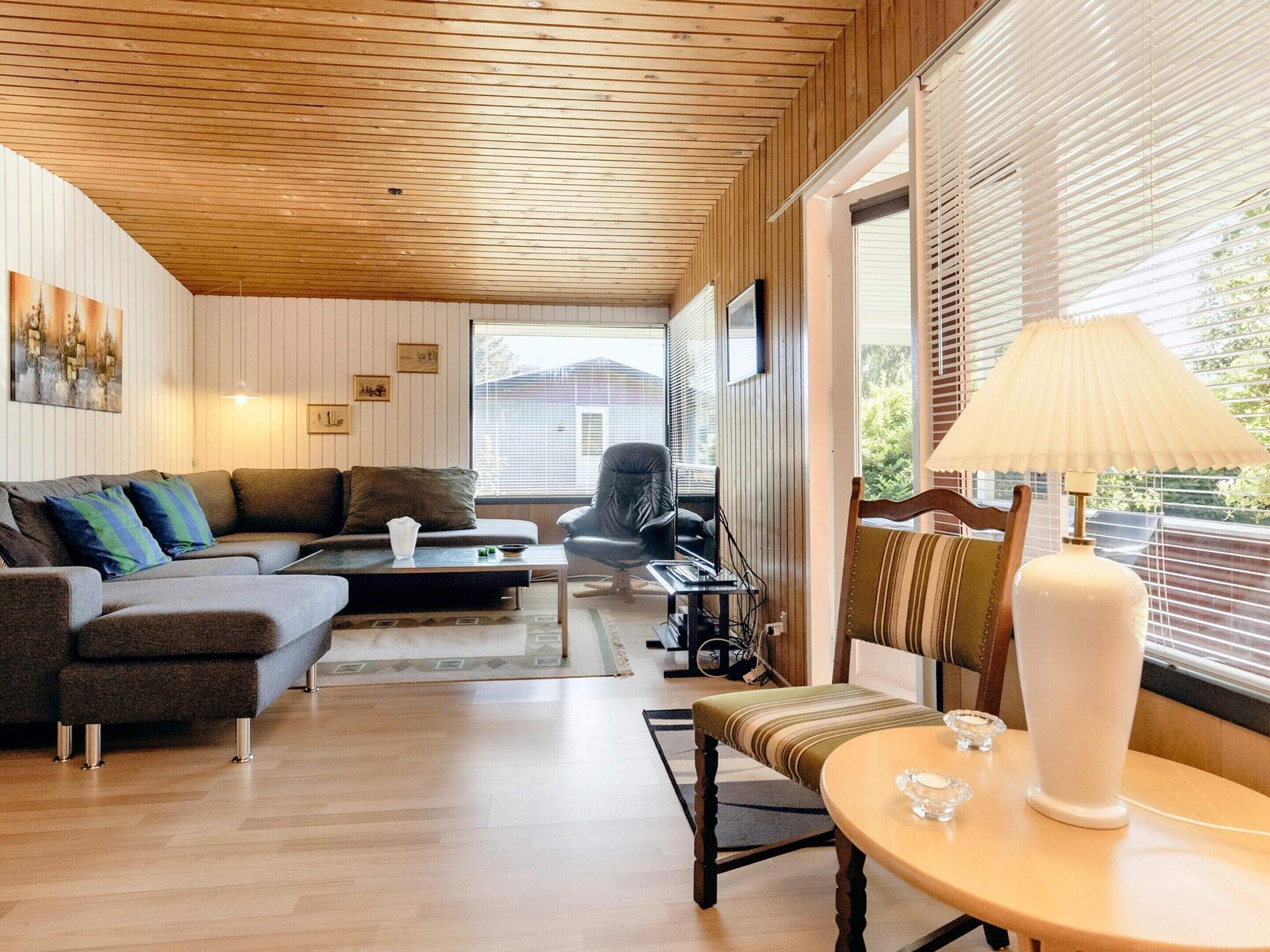 A modern living room with a wooden ceiling, a sofa, a dining table, and a chair.