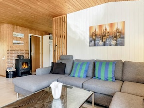 A cozy living room with a sectional sofa, a glass coffee table, a fireplace, and a wall-mounted painting.