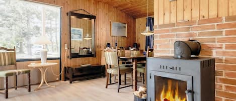 A cozy room with a fireplace, wooden walls, and a dining area.