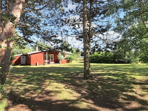 A red building with a porch, surrounded by trees and grass.