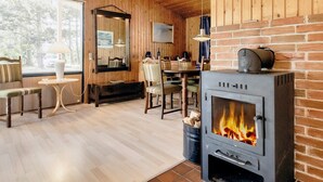 A cozy room with a fireplace, wooden walls, a dining area, and a large window.
