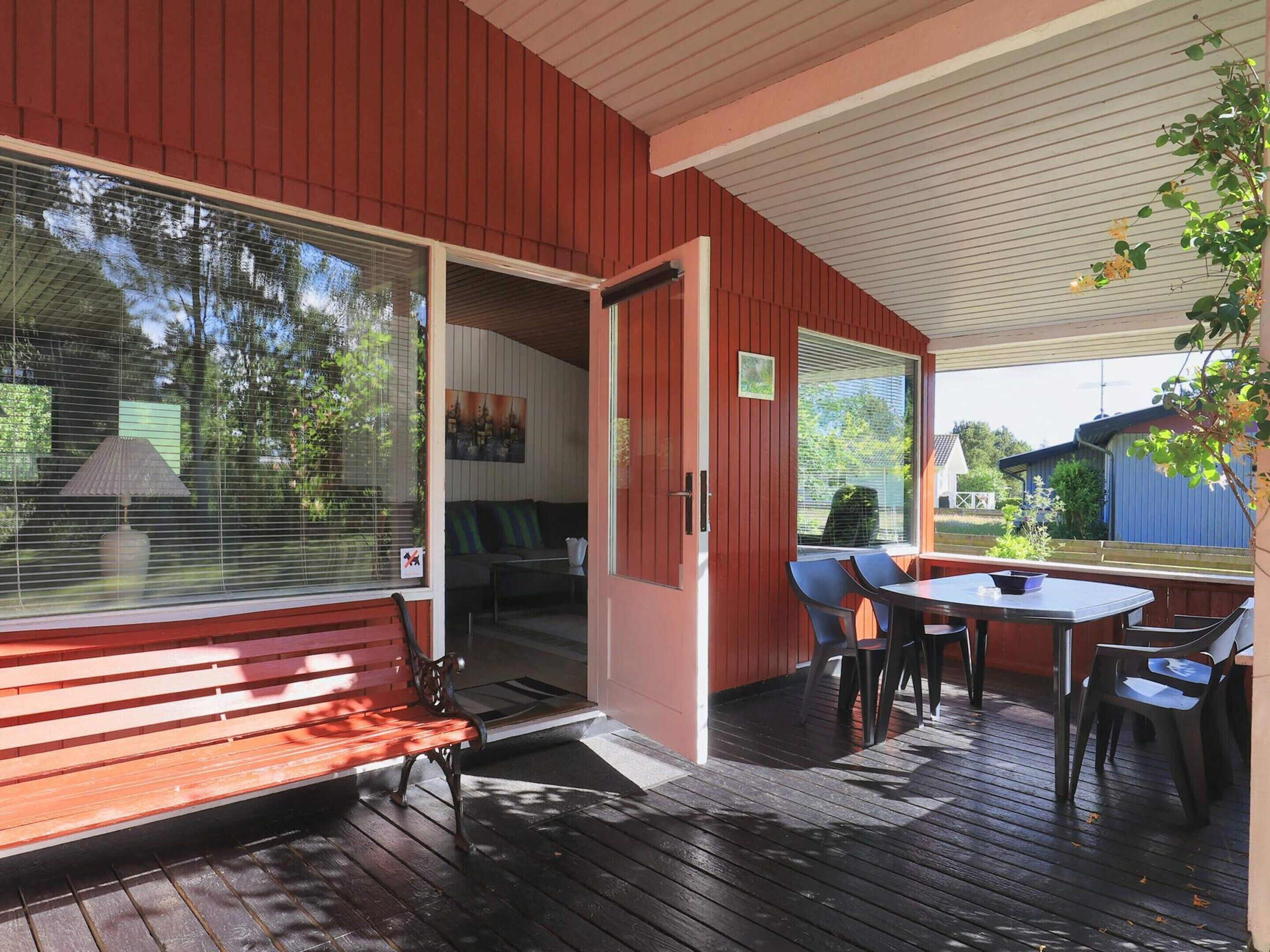 Un espacio exterior cubierto con un banco de madera, una mesa con sillas y vistas al entorno verde.