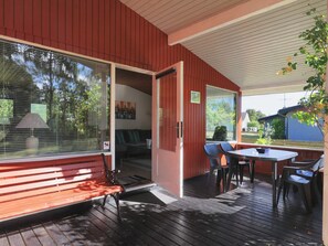 A covered outdoor area with a wooden bench, a table with chairs, and a view of the surrounding greenery.