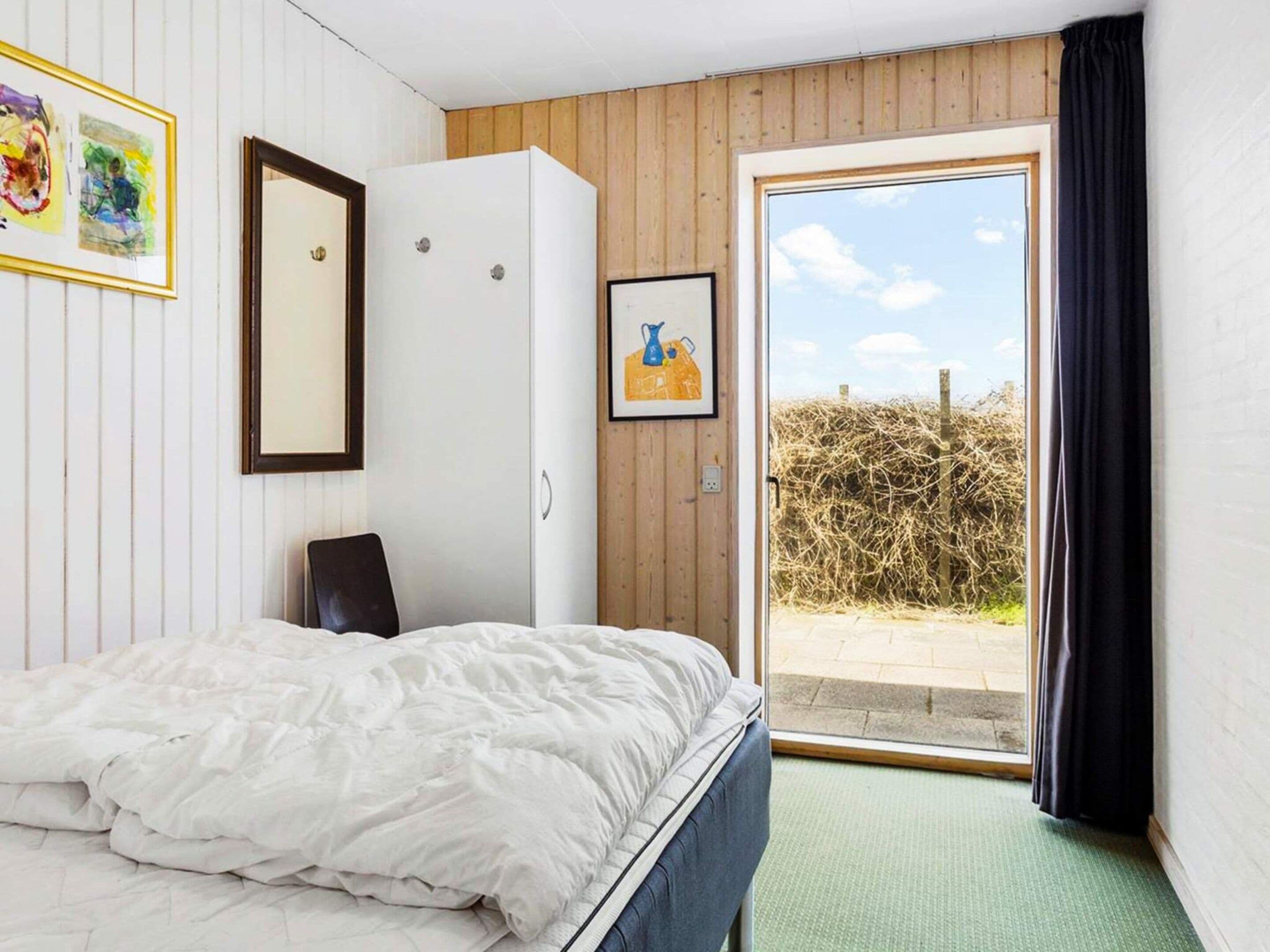 Een slaapkamer met een bed, een kledingkast, een raam met uitzicht en een deur naar een balkon.