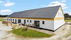 En etagers bygning med skråt tag, store vinduer og en lille have foran.