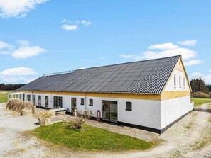 En enplansbyggnad med ett sluttande tak, stora fönster och en liten trädgårdsyta framför.