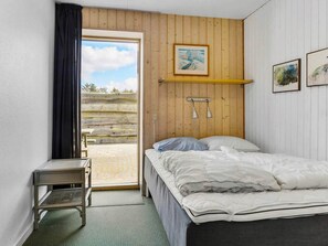 A bedroom with a bed, a bedside table, a window with curtains, a wooden wall, and a painting.