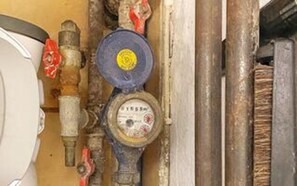 A close-up of a water meter with a yellow dial and a red valve.