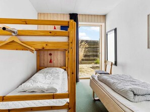 Une pièce avec deux lits superposés, une petite table et une chaise. Il y a une fenêtre qui donne sur l’extérieur.